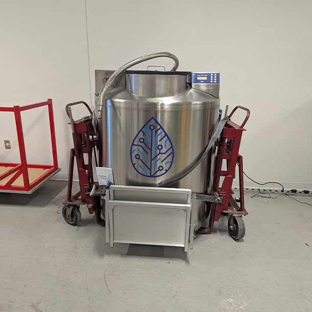 Large stainless steel liquid nitrogen biorepository tank secured on red mechanical dollies and ready for laboratory relocation