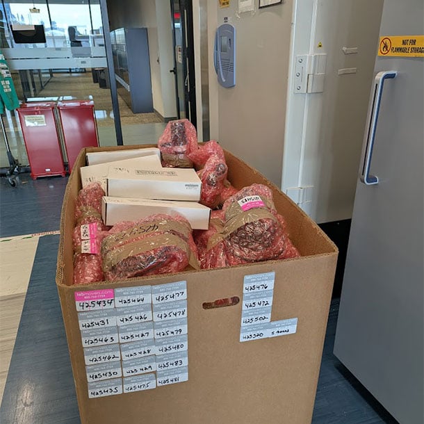 Open cardboard box filled with bubble-wrapped laboratory supplies, labeled with sequential Lab Movers inventory tracking numbers