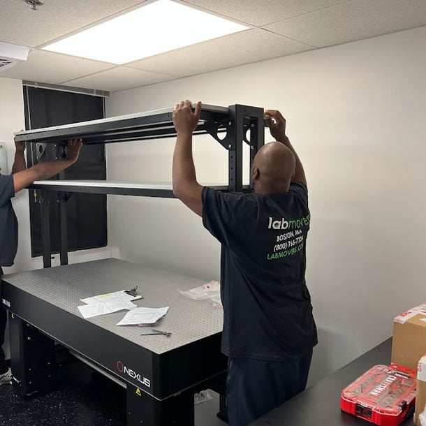 Lab Movers crew assembling and mounting an overhead rail superstructure onto a Nexus optical table in a newly built research laboratory